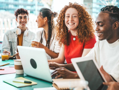 Multiracial university students sitting together at table with books and laptop - Happy young people doing group study in high school library - Life style concept with guys and girls in college campus