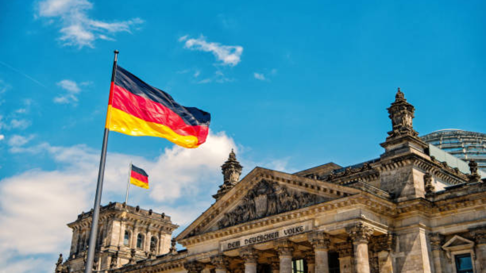 German flags waving in the wind at famous Reichstag building, seat of the German Parliament Deutscher Bundestag , on a sunny day with blue sky and clouds, central Berlin Mitte district, Germany